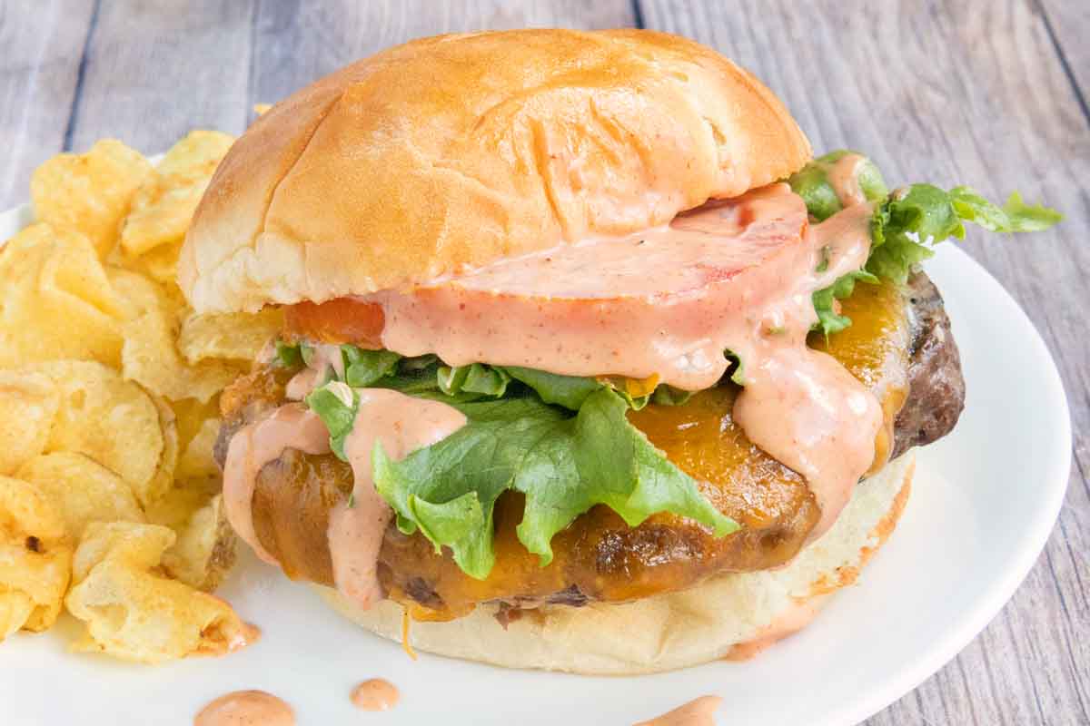 Cheeseburger with lettuce, tomato and burger sauce on a white plate.