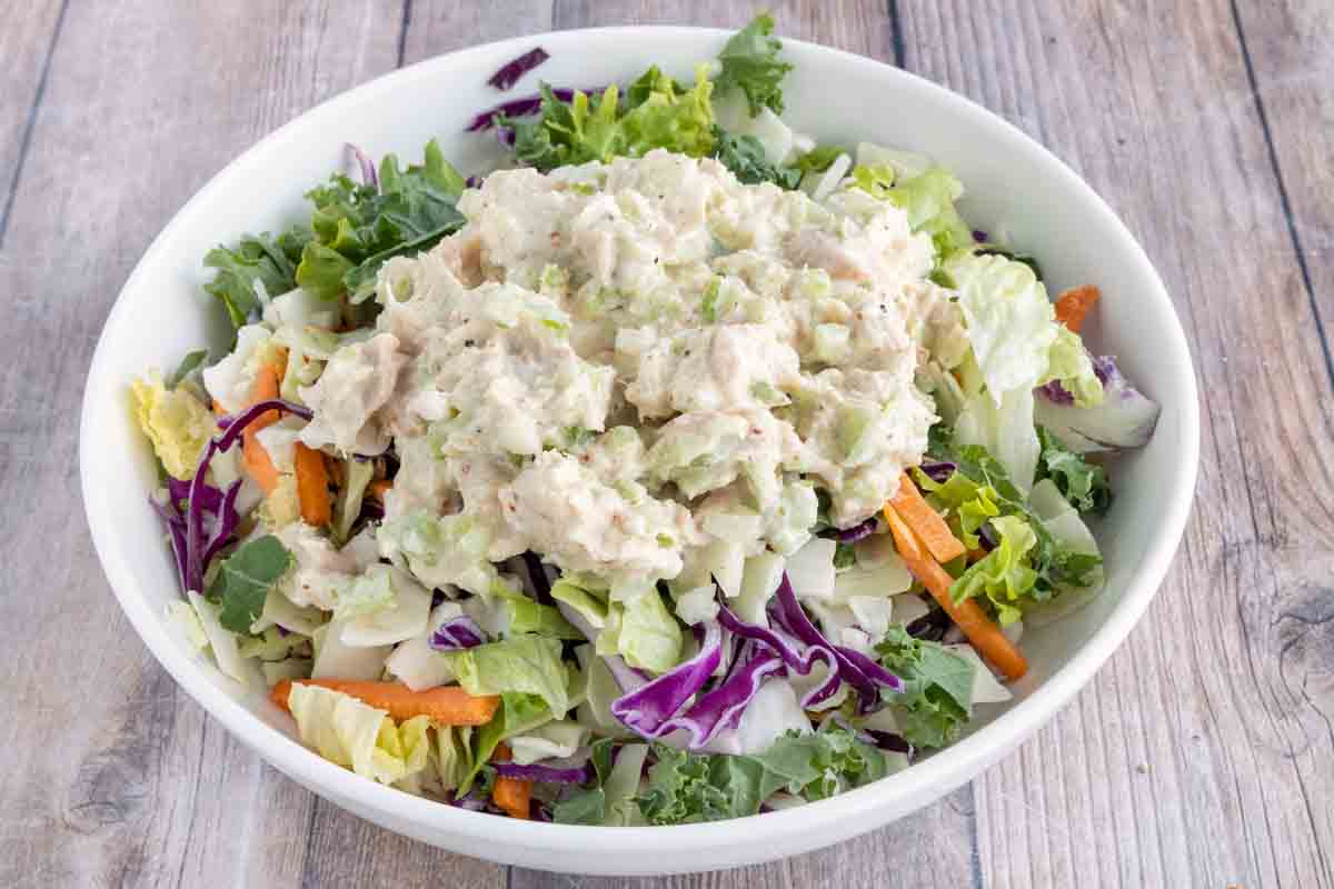 Tuna salad on top of tossed salad in a white bowl.