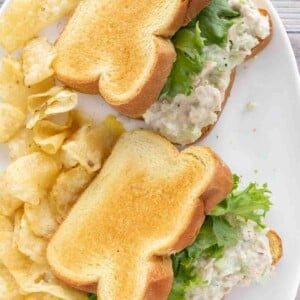 two tuna salad sandwiches with potato chips on a white platter.
