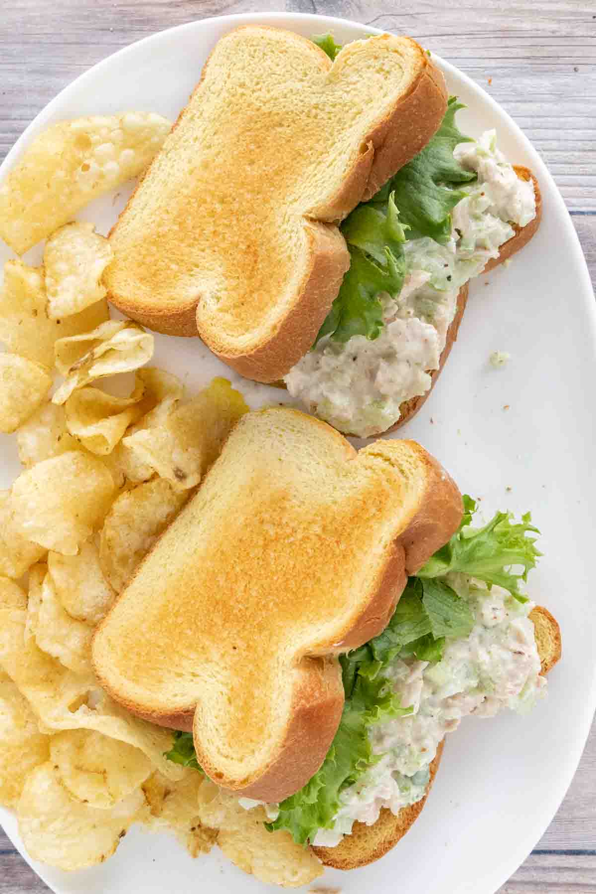 two tuna salad sandwiches with potato chips on a white platter.
