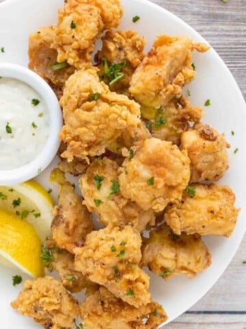 Catfish nuggets on a. white plate with tarter sauce and lemons.
