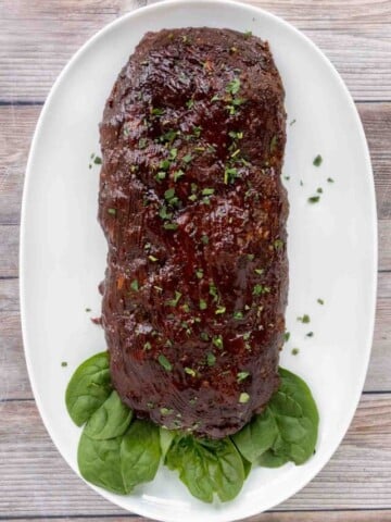 Smoked meatloaf on a white platter with spinach leaves.