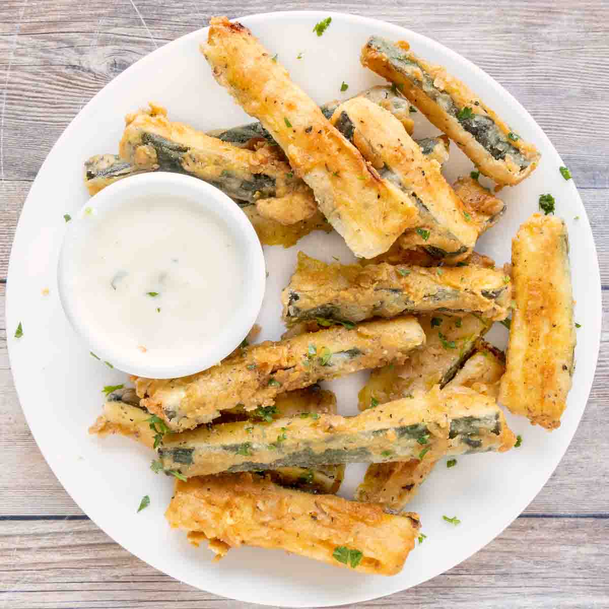 Fried zucchini sticks on a white platter with dipping sauce.