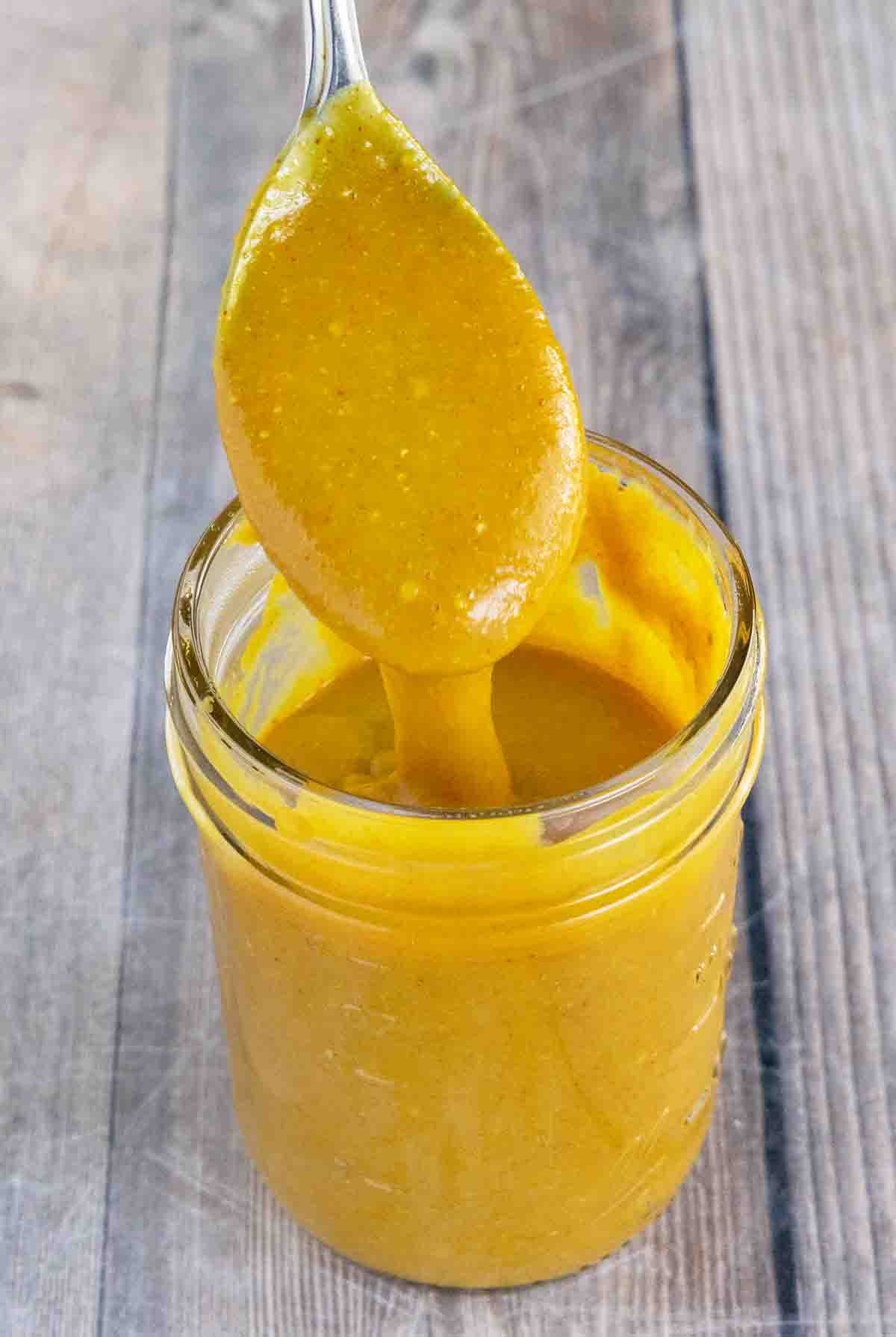 Carolina Gold bbq sauce in a glass jar with a spoon coming out.