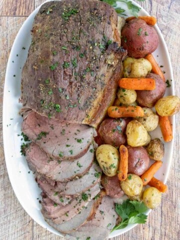 Sliced eye round of roast with potatoes and carrots on a white platter.