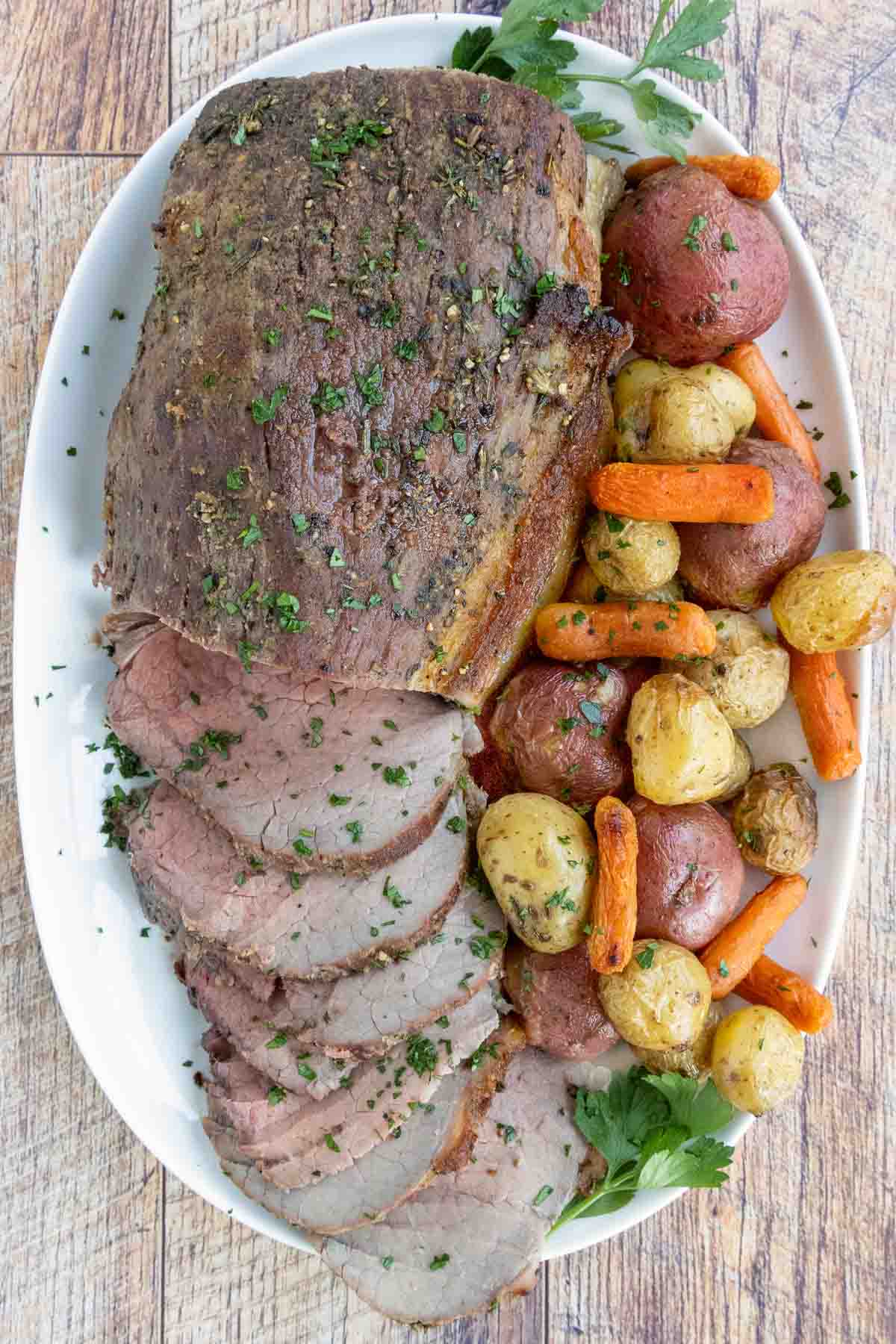 Sliced eye round of roast with potatoes and carrots on a white platter.