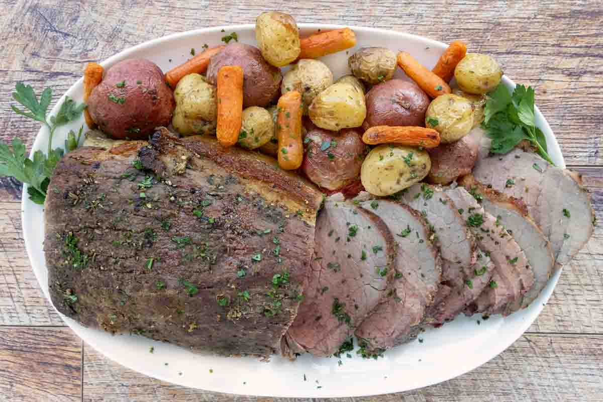 Sliced eye round of roast with potatoes and carrots on a white platter.