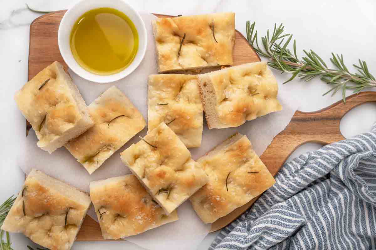 slices of focaccia bread on white marble with sprig of rosemary and small bowl of olive oil.