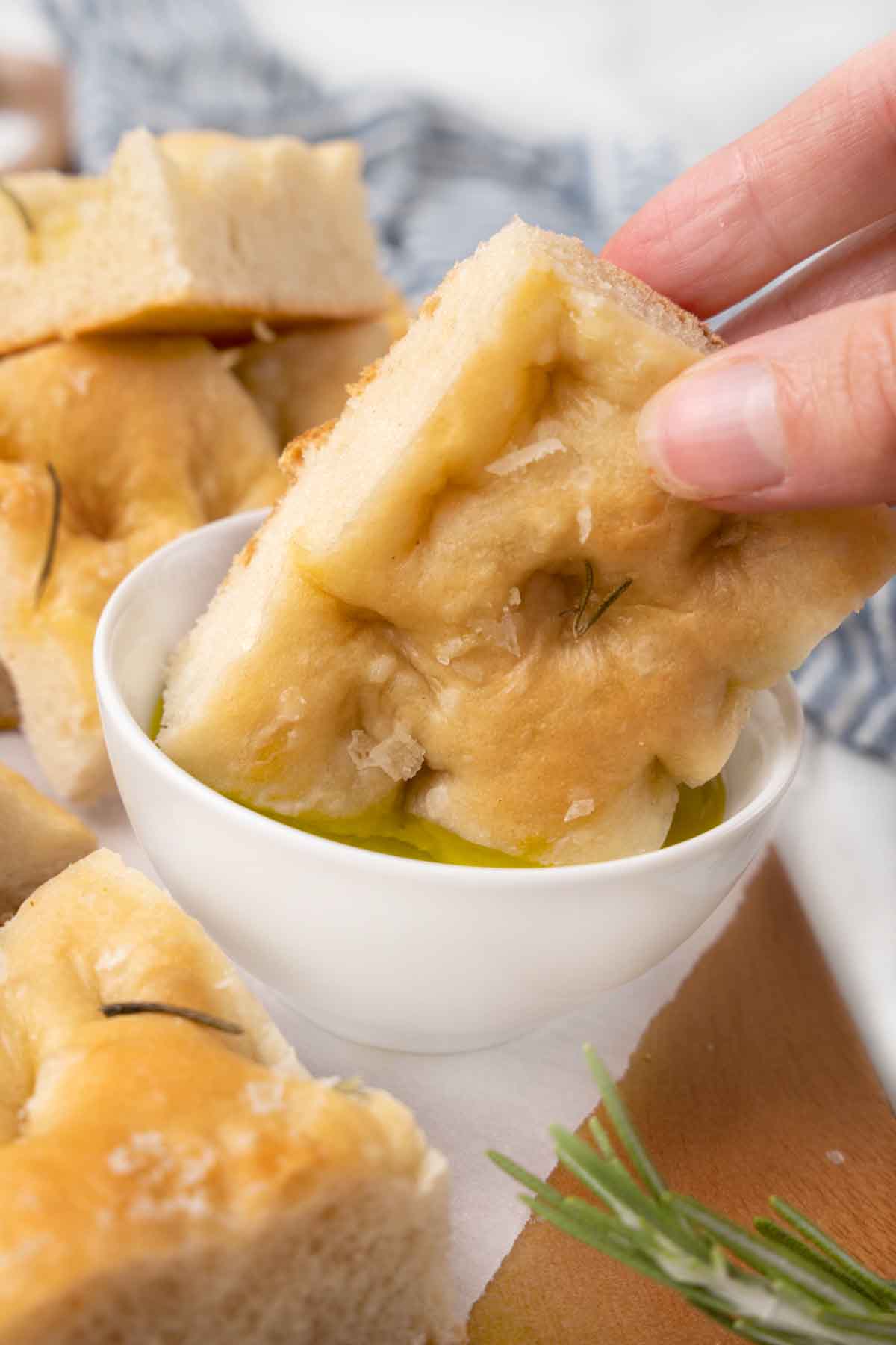 Hand dipping slice of focaccia into a white bowl of olive oil.