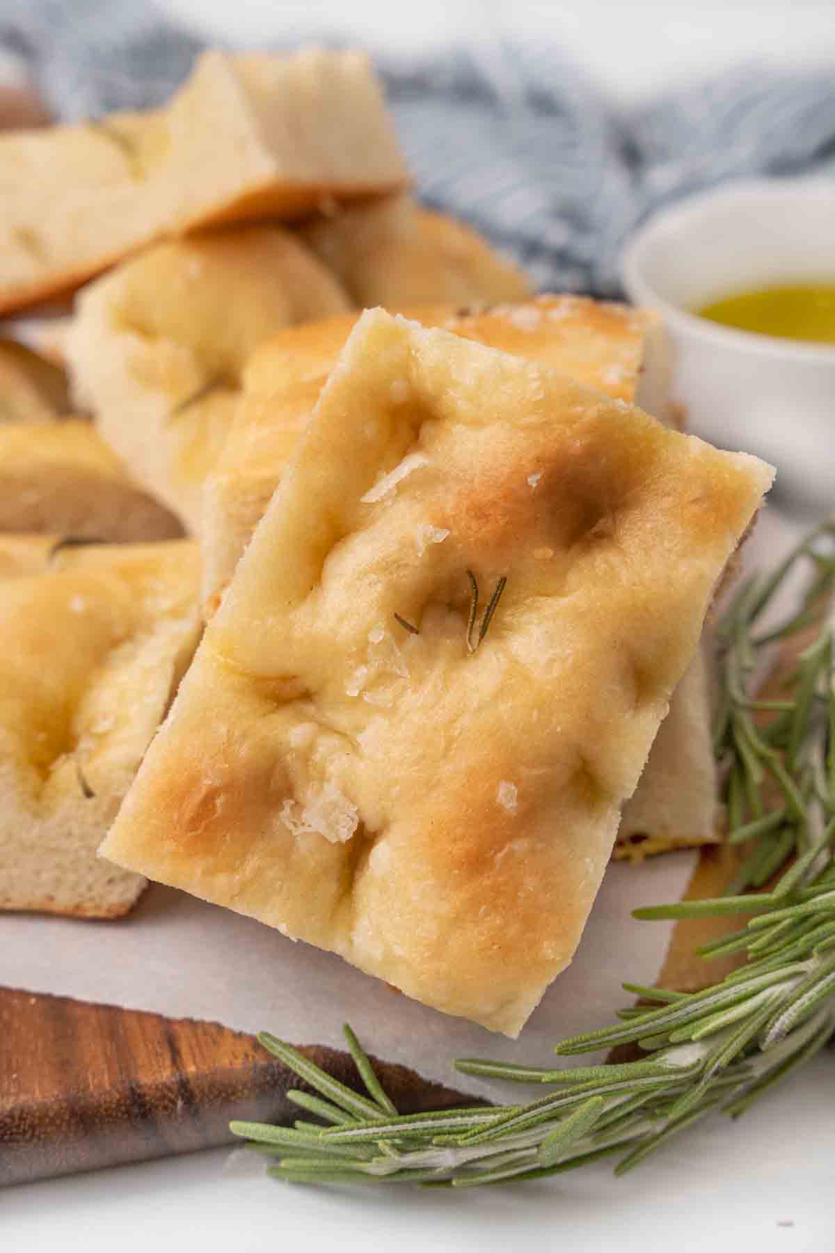 Slices of focaccia bread with sprig of rosemary on a brown cutting board.