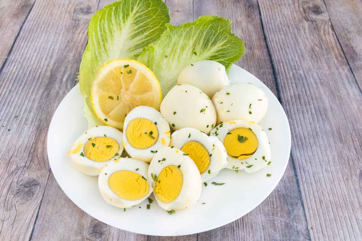 Smoked eggs whole and halves on a white plate with romaine leaves and lemons.