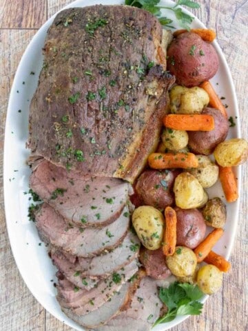 Sliced eye round of roast with potatoes and carrots on a white platter.