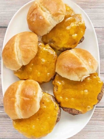 Smoked burgers with cheese on buns on a white platter.