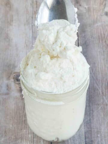 Homemade whipped cream in a jar with a spoon coming out.