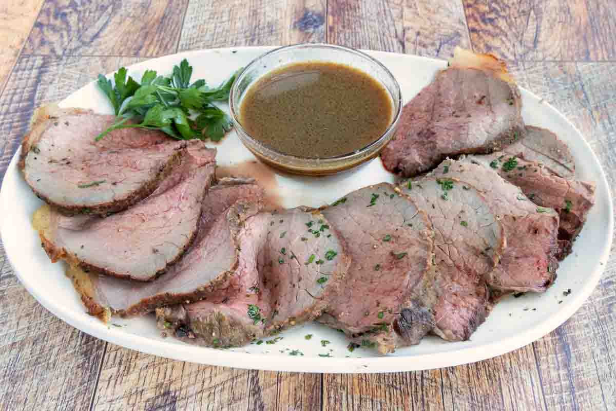 Sliced eye round of roast with au jus on a white platter.