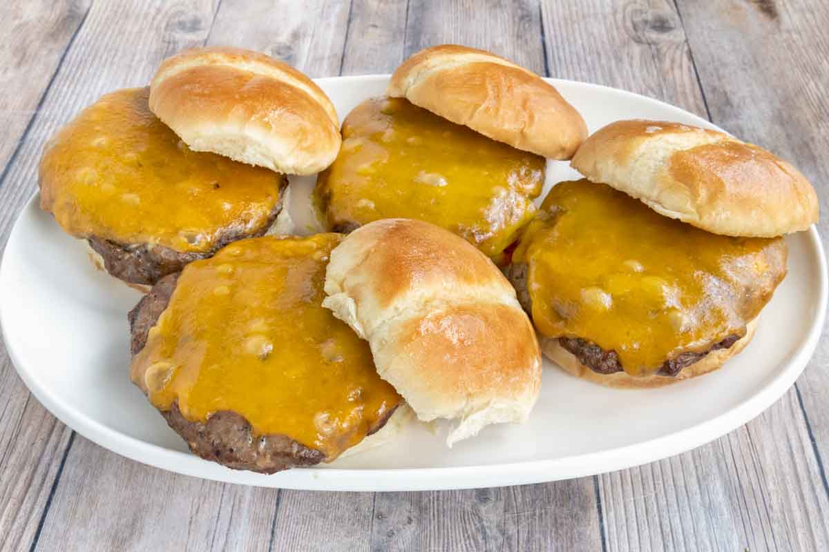 Smoked burgers with cheese on buns on a white platter.