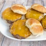 Smoked burgers with cheese on buns on a white platter.