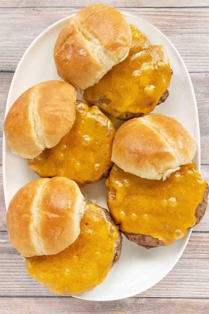 Smoked burgers with cheese on buns on a white platter.