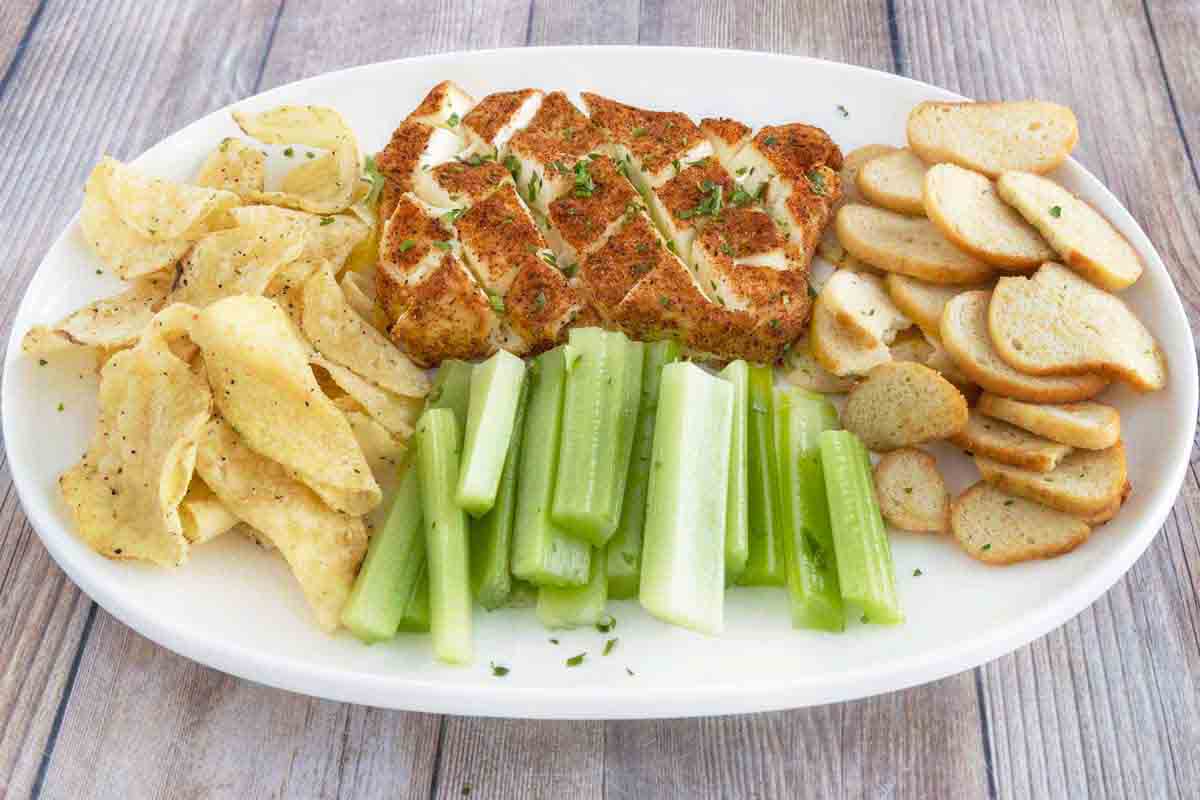 Smoked cream cheese with chips, toasts and celery on a white platter.