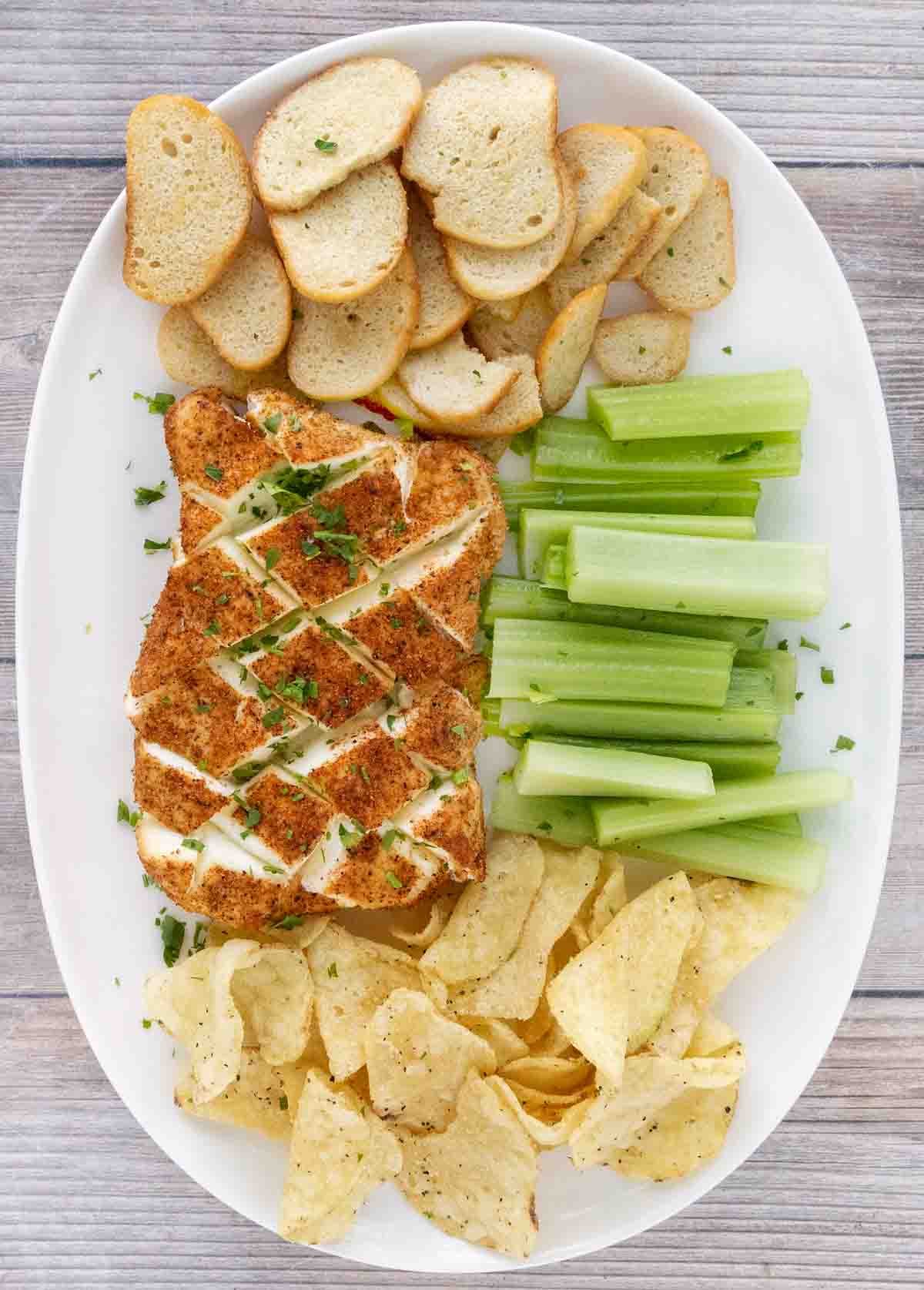 Smoked cream cheese with chips, toasts and celery on a white platter.