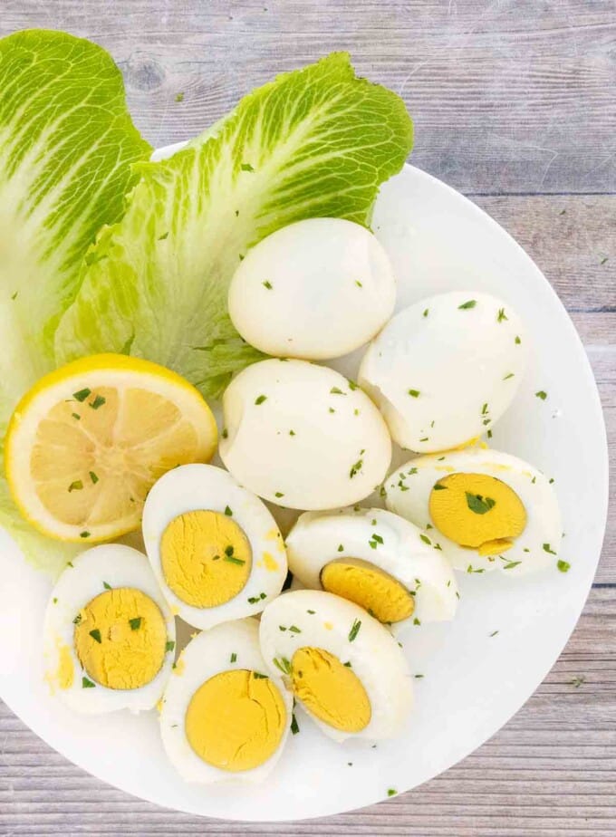 Smoked eggs whole and halves on a white plate with romaine leaves and lemons.