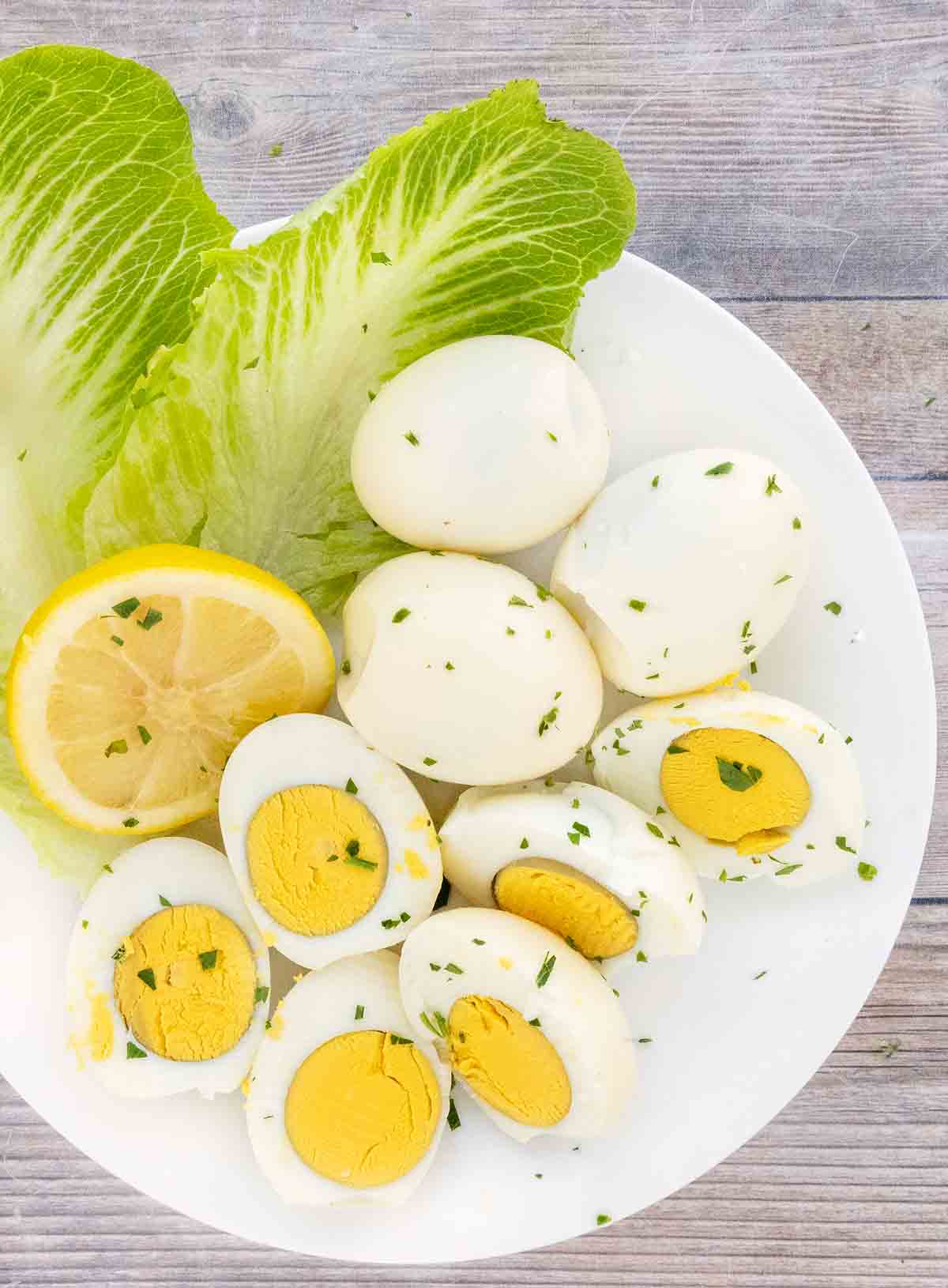 Smoked eggs whole and halves on a white plate with romaine leaves and lemons.