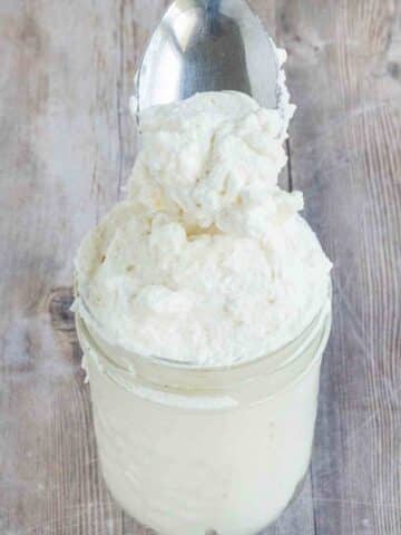 Homemade whipped cream in a jar with a spoon coming out.