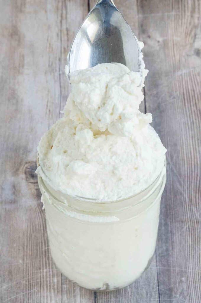 Homemade whipped cream in a jar with a spoon coming out.