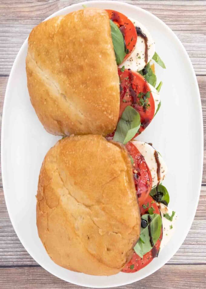 Two Caprese sandwiches on a white platter.