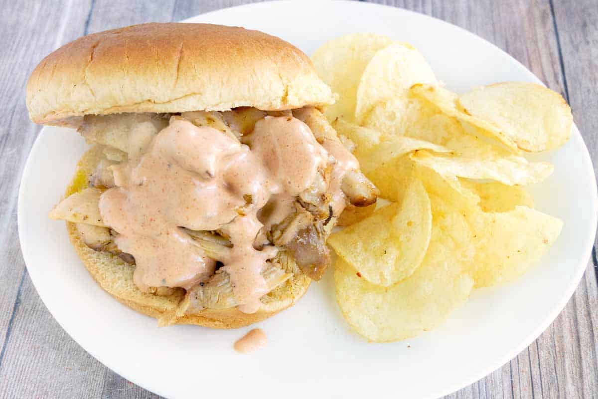 Comeback sauce on a pulled chicken sandwich on a white plate with chips.