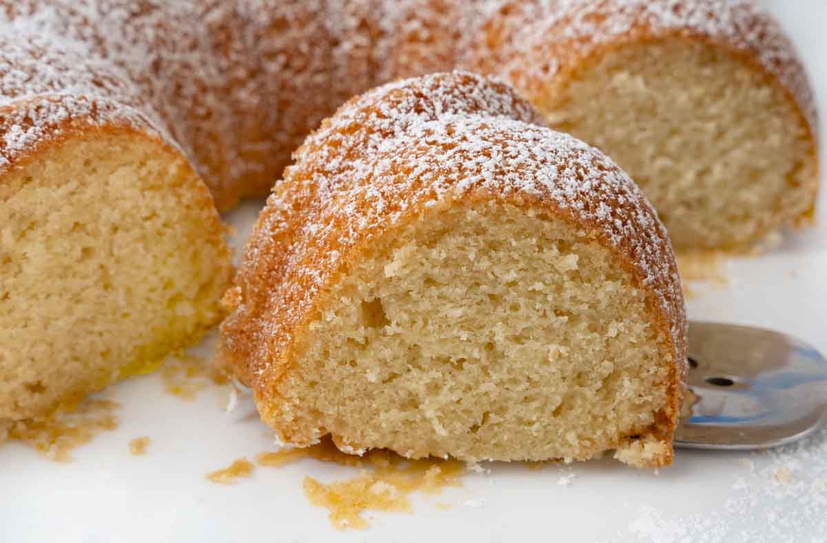 Slice of Vanilla Bundt Cake in front of the rest of the cake on a white platter.