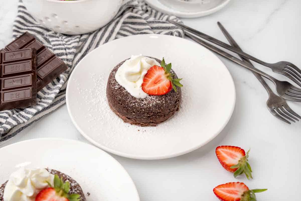 Lava cake topped with whipped cream and a strawberry slice on a white plate.