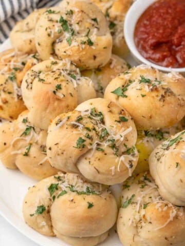 Garlic knots on a white platter with a bowl of marinara sauce.