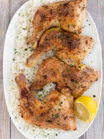 Four honey garlic chicken quarters on a white platter over a bed of white rice.