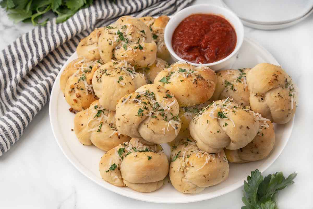 Garlic knots on a white platter with a bowl of marinara sauce.