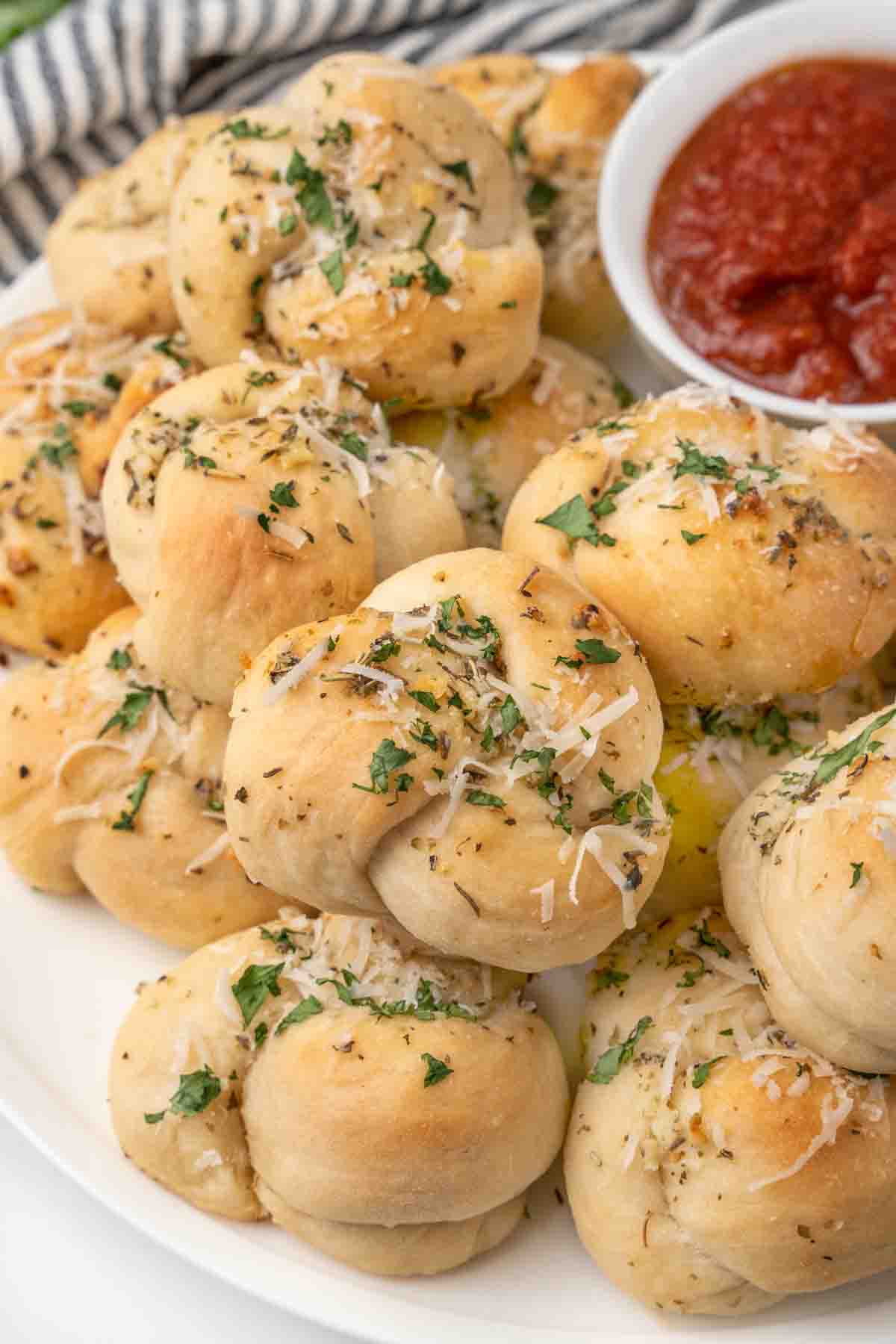 Garlic knots on a white platter with a bowl of marinara sauce.