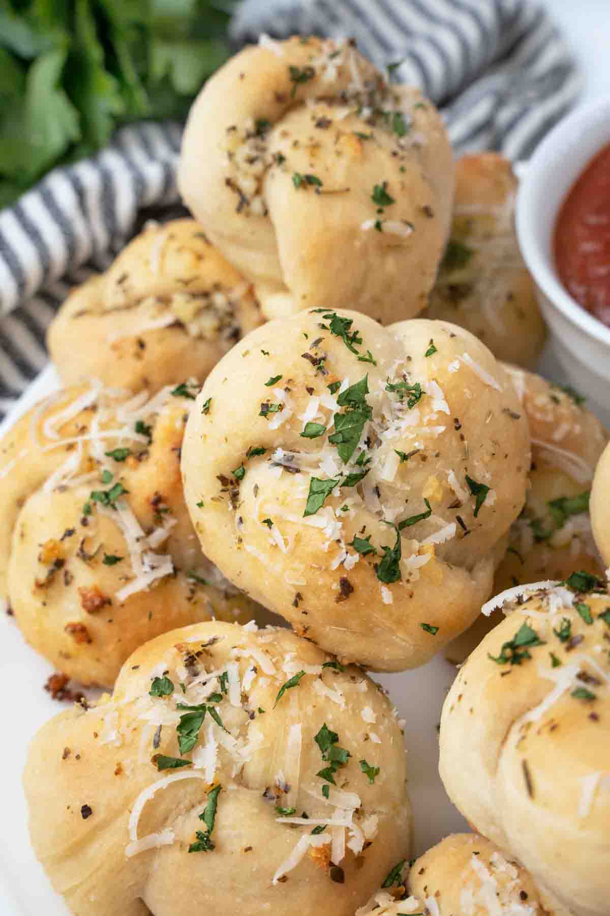 Garlic knots on a white platter with a bowl of marinara sauce.