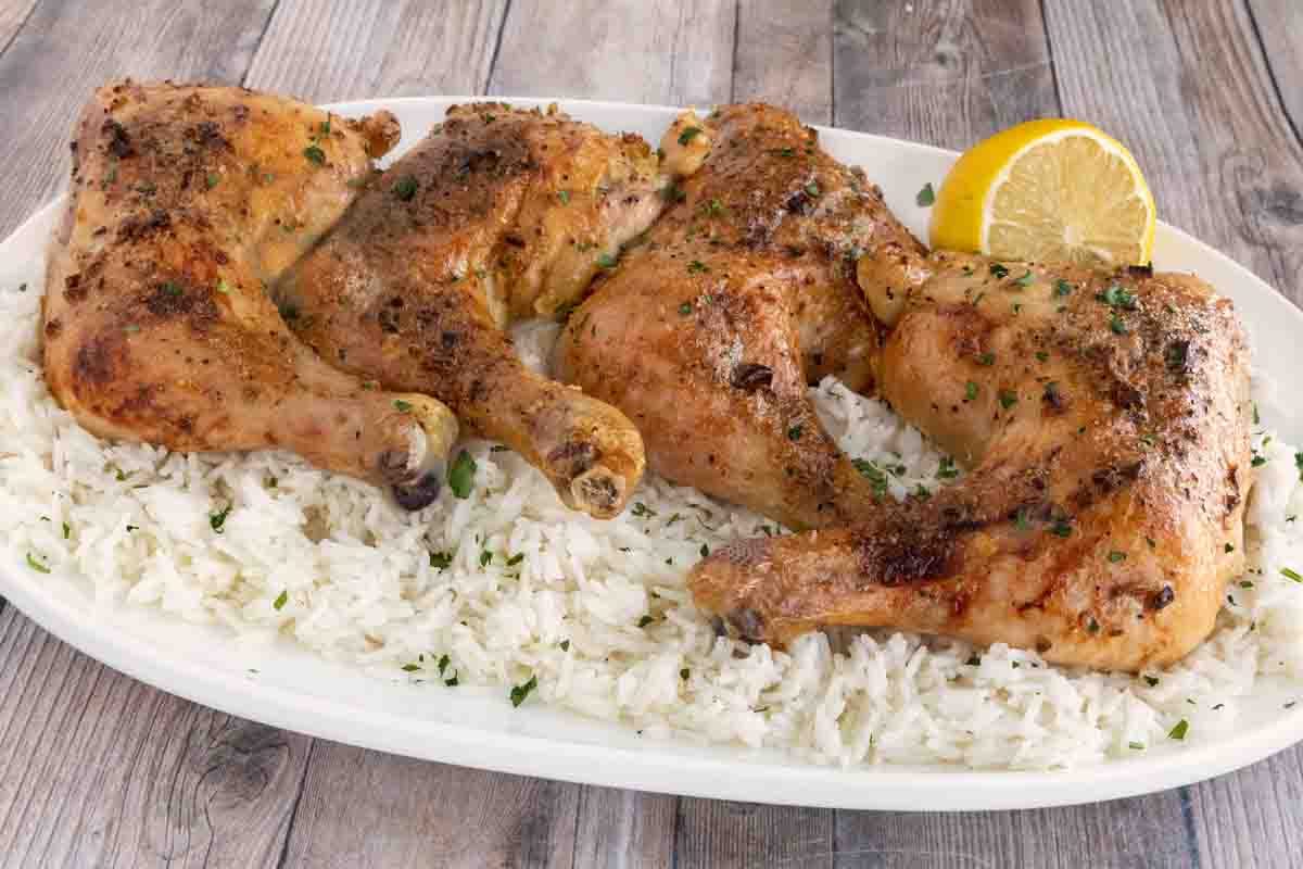 Four honey garlic chicken quarters on a white platter over a bed of white rice.