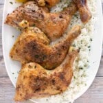 Honey garlic chicken quarters on a white platter over a bed of white rice.