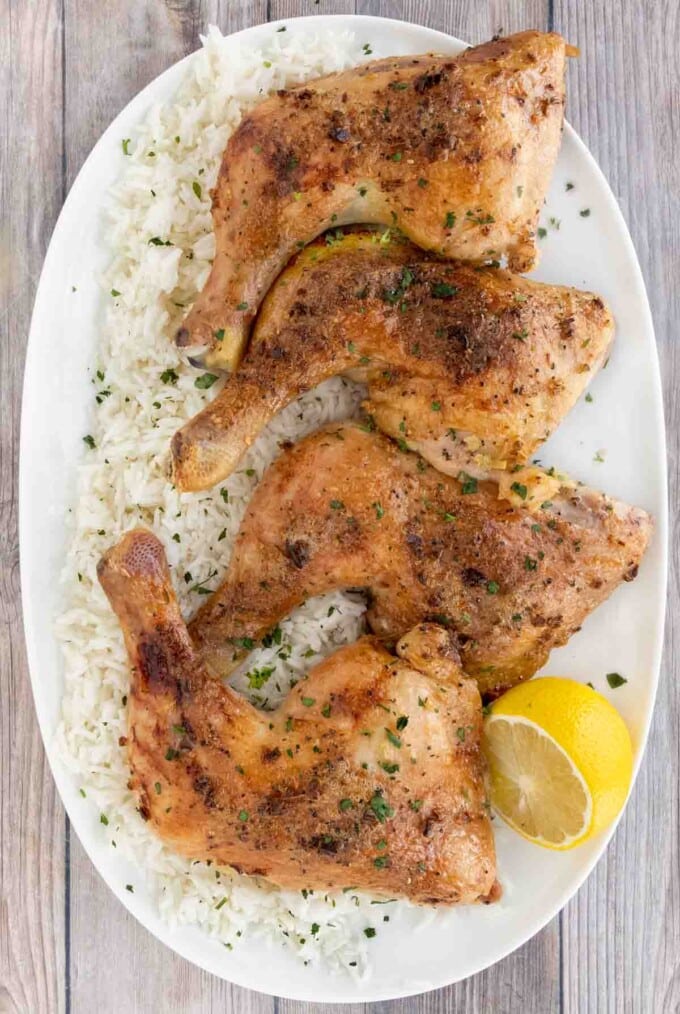 Four honey garlic chicken quarters on a white platter over a bed of white rice.