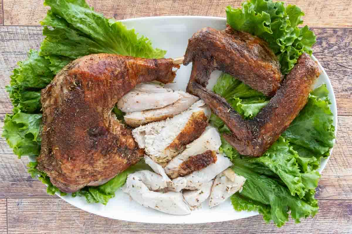 Brined turkey legs, wings and sliced breast on a white platter.