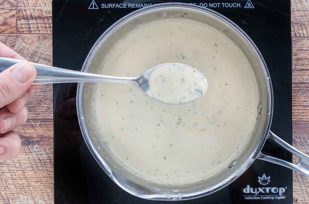 Finished garlic parmesan sauce in a saucepan with a spoon holding the sauce.