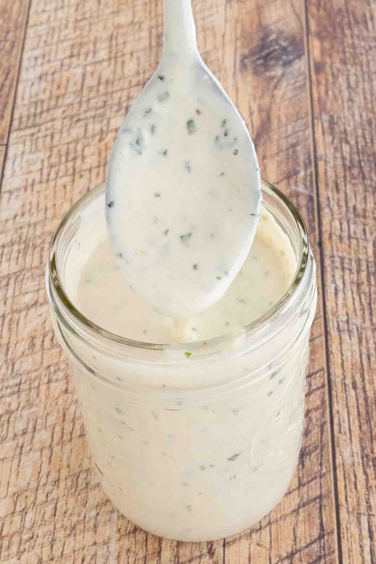 Garlic parmesan sauce in a glass jar with a spoon coming out.