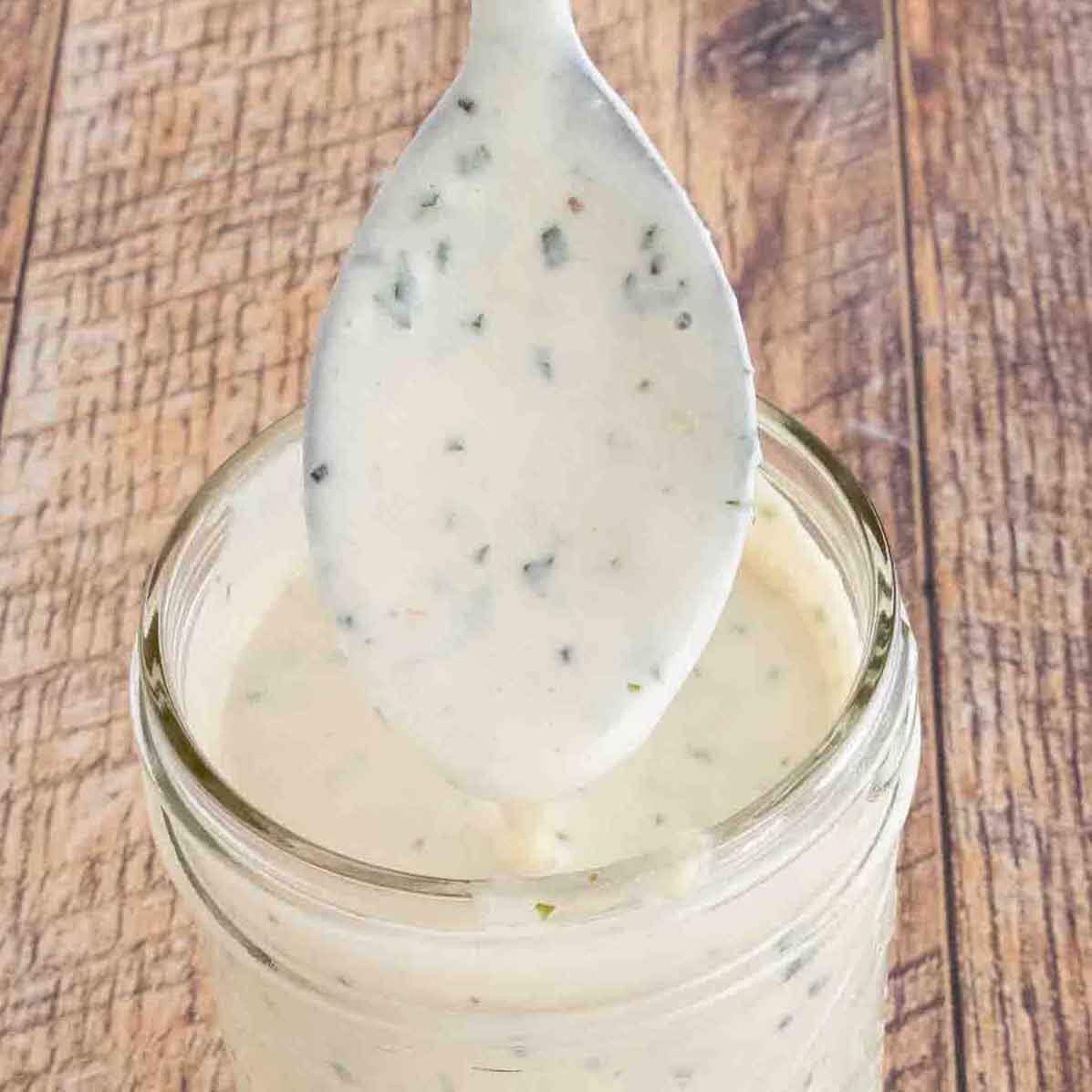 Garlic parmesan sauce in a glass jar with a spoon coming out.