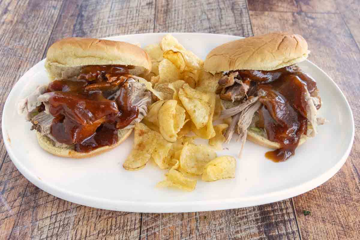 Two pulled pork sandwiches with Memphis Barbecue Sauce and potato chips on a white platter.