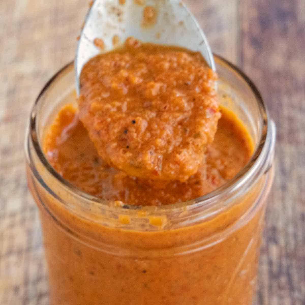 Peri-Peri Sauce in a glass jar with a spoon coming out of the jar.