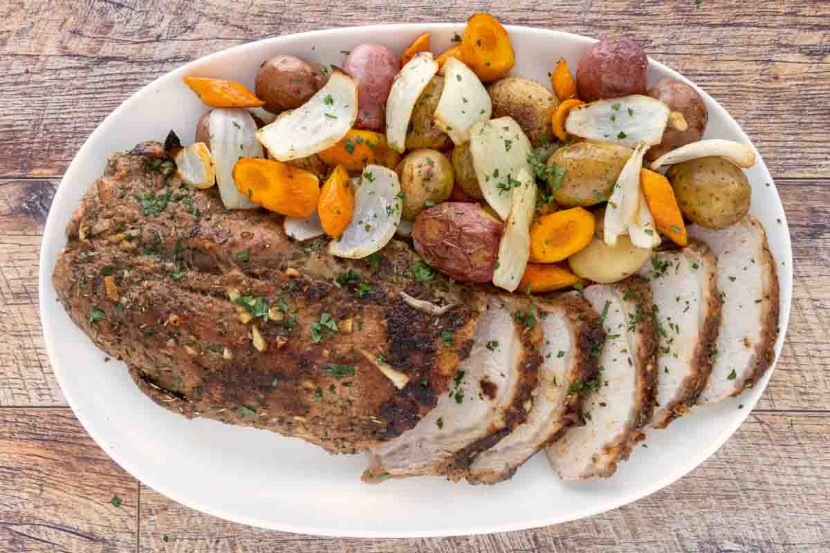 Sliced roasted pork loin with vegetables on a white platter.