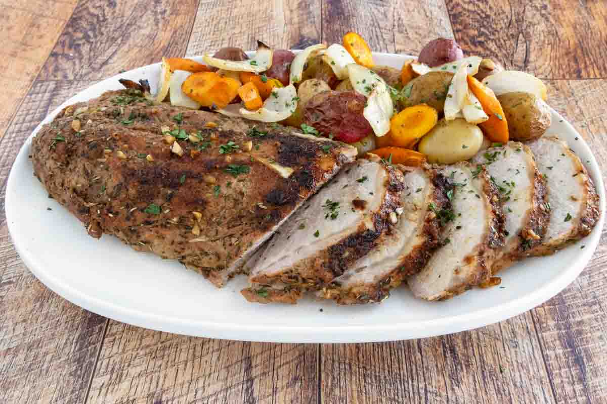 Sliced roasted pork loin with vegetables on a white platter.