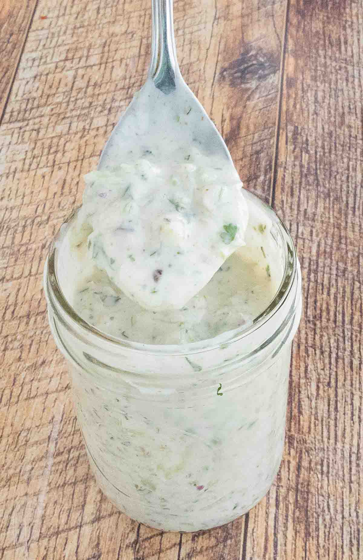 Raita sauce in a glass jar with a spoon coming out.