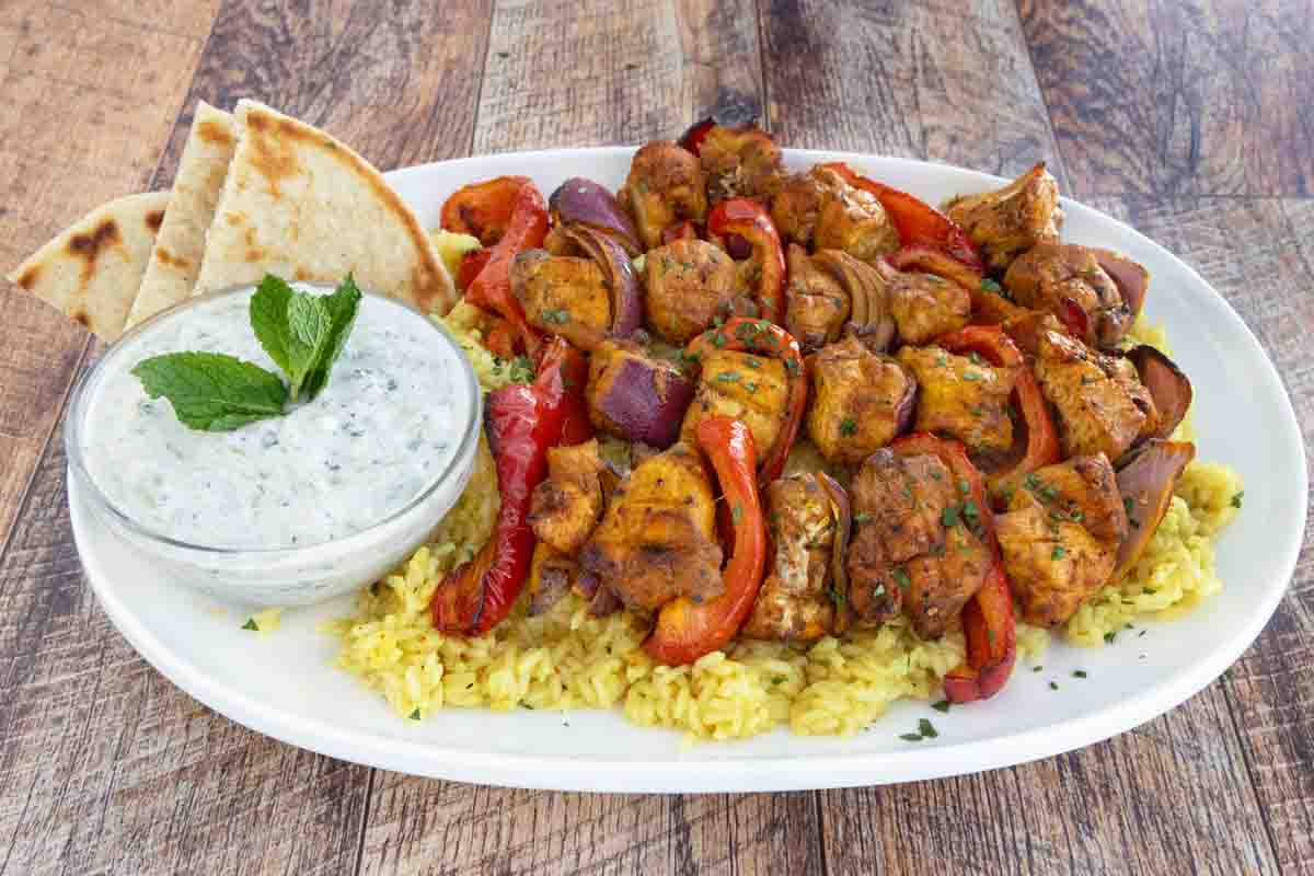 Raita Sauce with chicken skewers on a white platter.